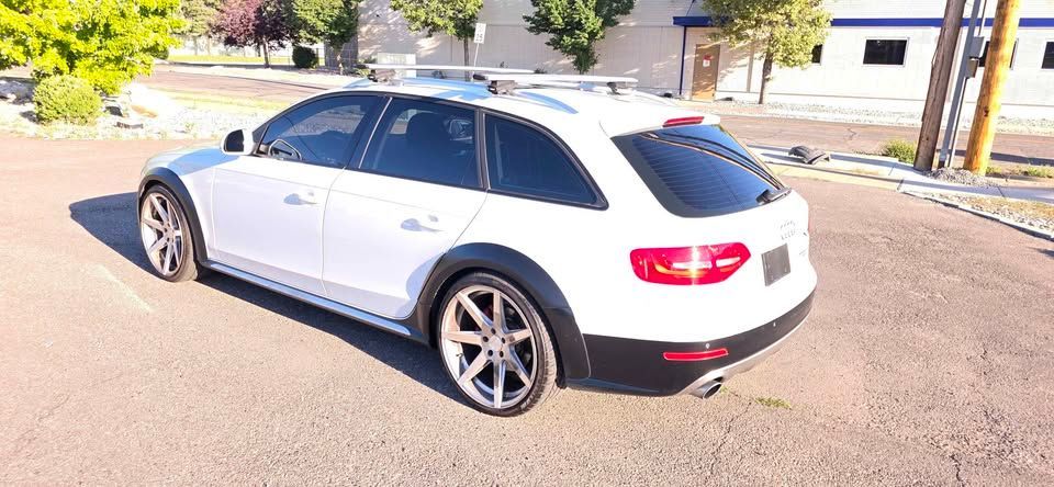 White Audi wagon parked on a sunlit street near buildings and trees.