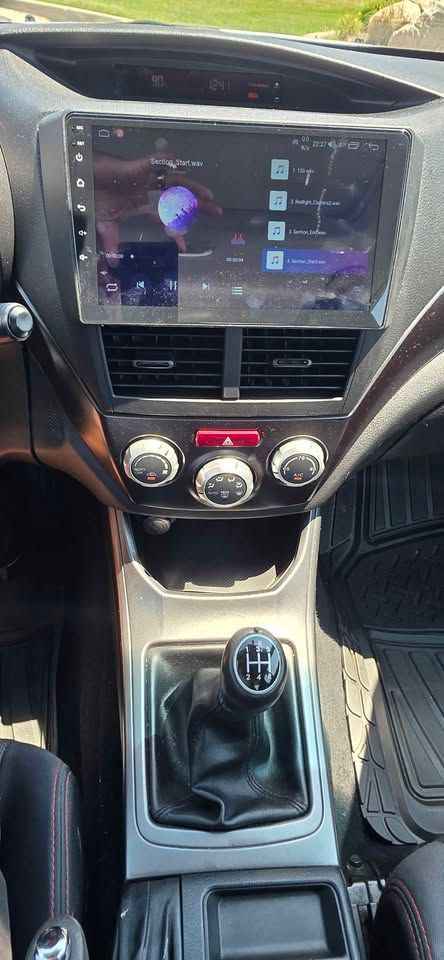 Car dashboard with touchscreen, climate controls, and manual gear shift visible in center console.