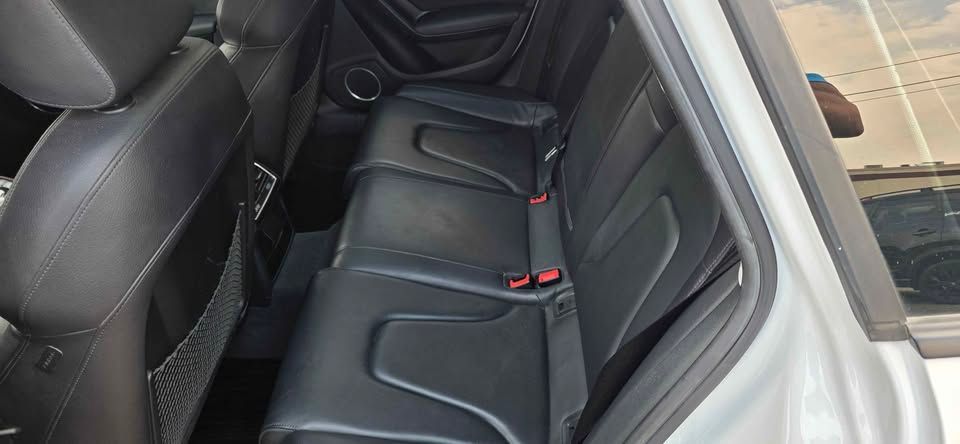 Black leather car back seat with red seatbelt buckles and folded center armrest, viewed through an open door