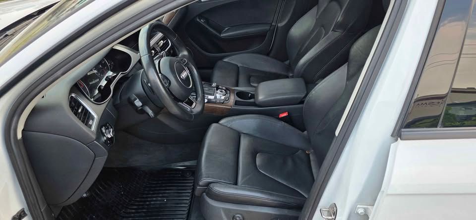Car interior with black leather seats, steering wheel, and open driver’s door, viewed from outside
