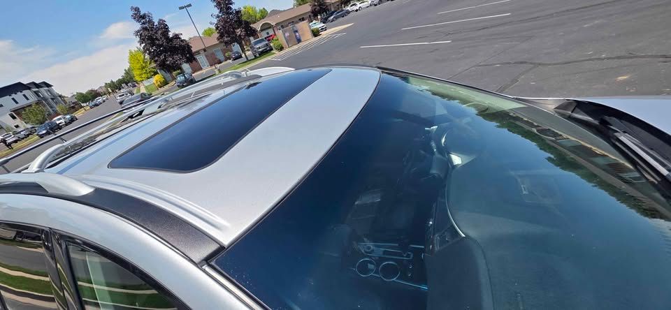 Silver car roof with a black sunroof parked in a lot under a clear sky