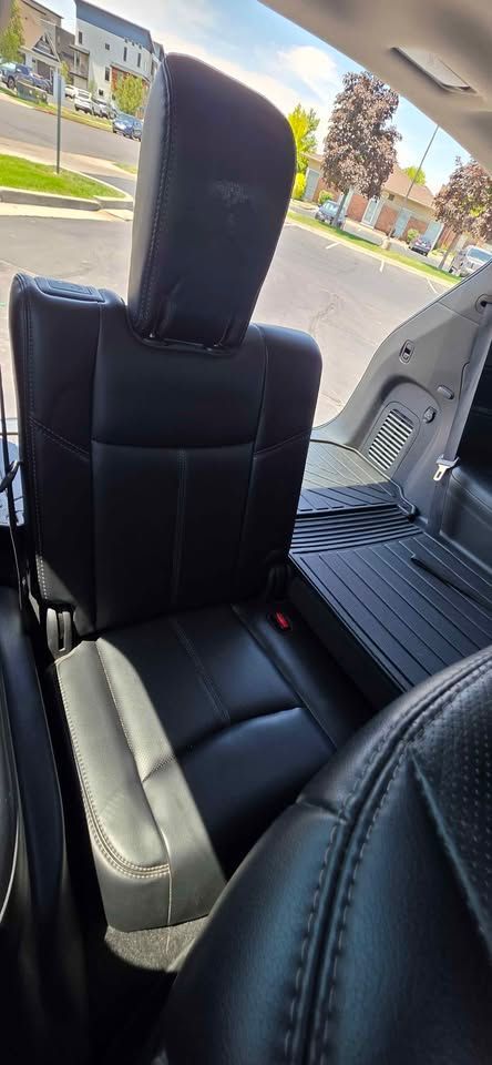 Black leather rear car seat with a headrest and visible seatbelt in a vehicle interior.