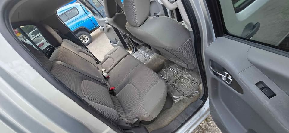 Open car door showing gray cloth rear seats and interior, with a blue dashboard visible ahead