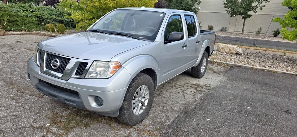 Silver Nissan pickup truck parked on a gravel lot near a building and trees