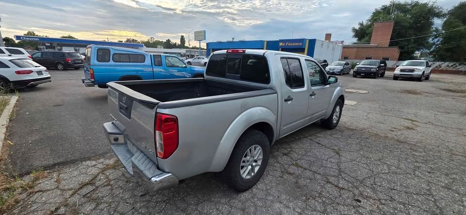 Silver pickup truck parked in a lot beside other vehicles and a blue van at dusk