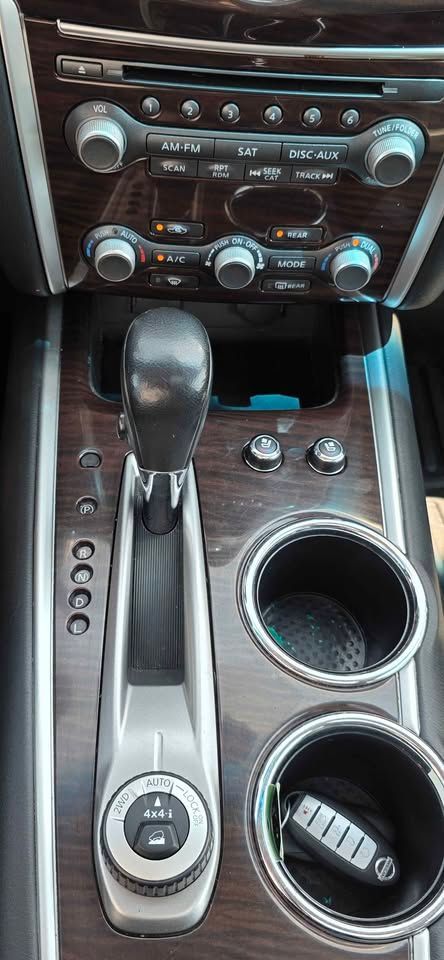 Car center console with gear shifter, climate controls, buttons, and two cup holders.