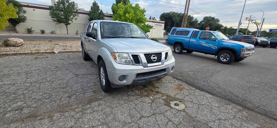 Silver Nissan SUV in a cracked parking lot beside a blue pickup truck, near a white building.
