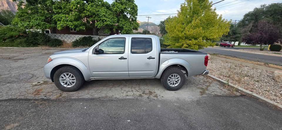 Silver pickup truck parked on a gravel lot beside a road, with trees in the background