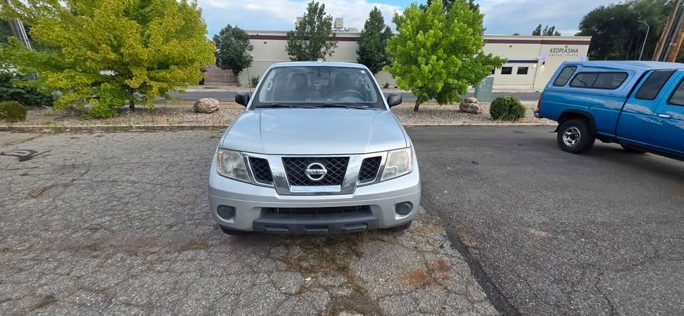 Silver Nissan SUV parked on a cracked lot with trees and a blue truck in the background.