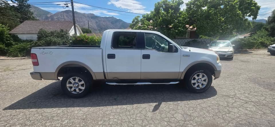 White pickup truck parked on a gravel lot with mountains and trees in the background