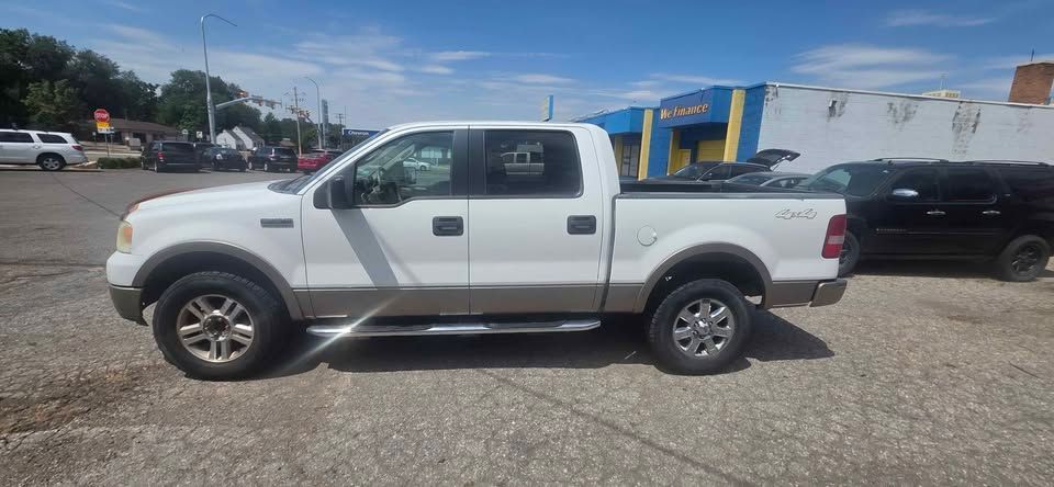 Silver pickup truck parked on gravel lot beside a black SUV and a blue building