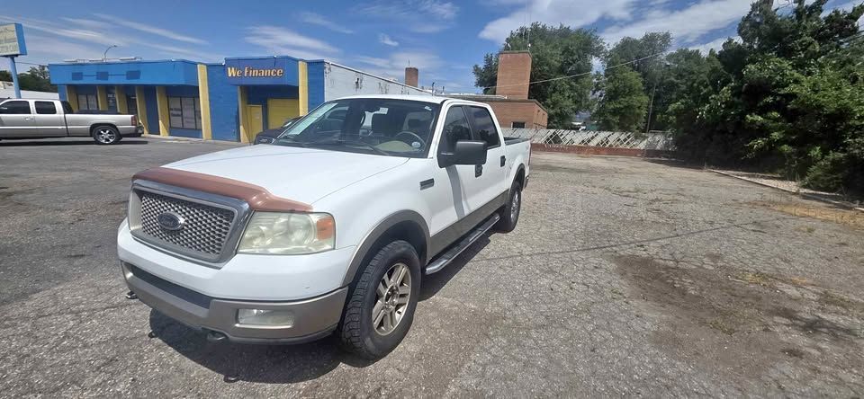 White pickup truck parked on a gravel lot beside a blue building under a sunny sky