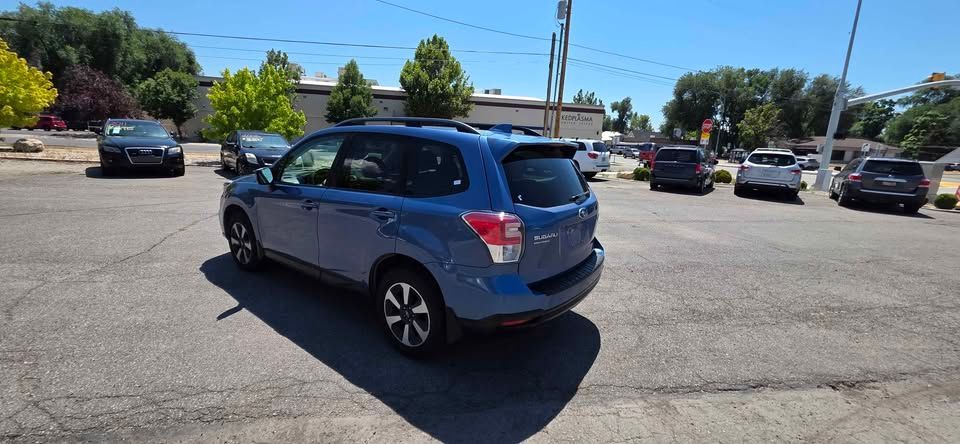Blue hatchback car parked in a sunny lot with other cars and trees in the background