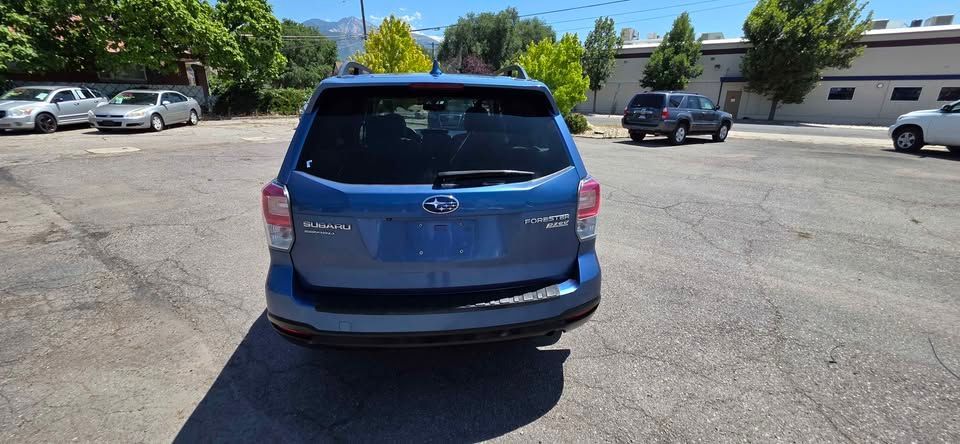 Blue SUV parked in a sunlit parking lot, rear view with trees and other cars nearby