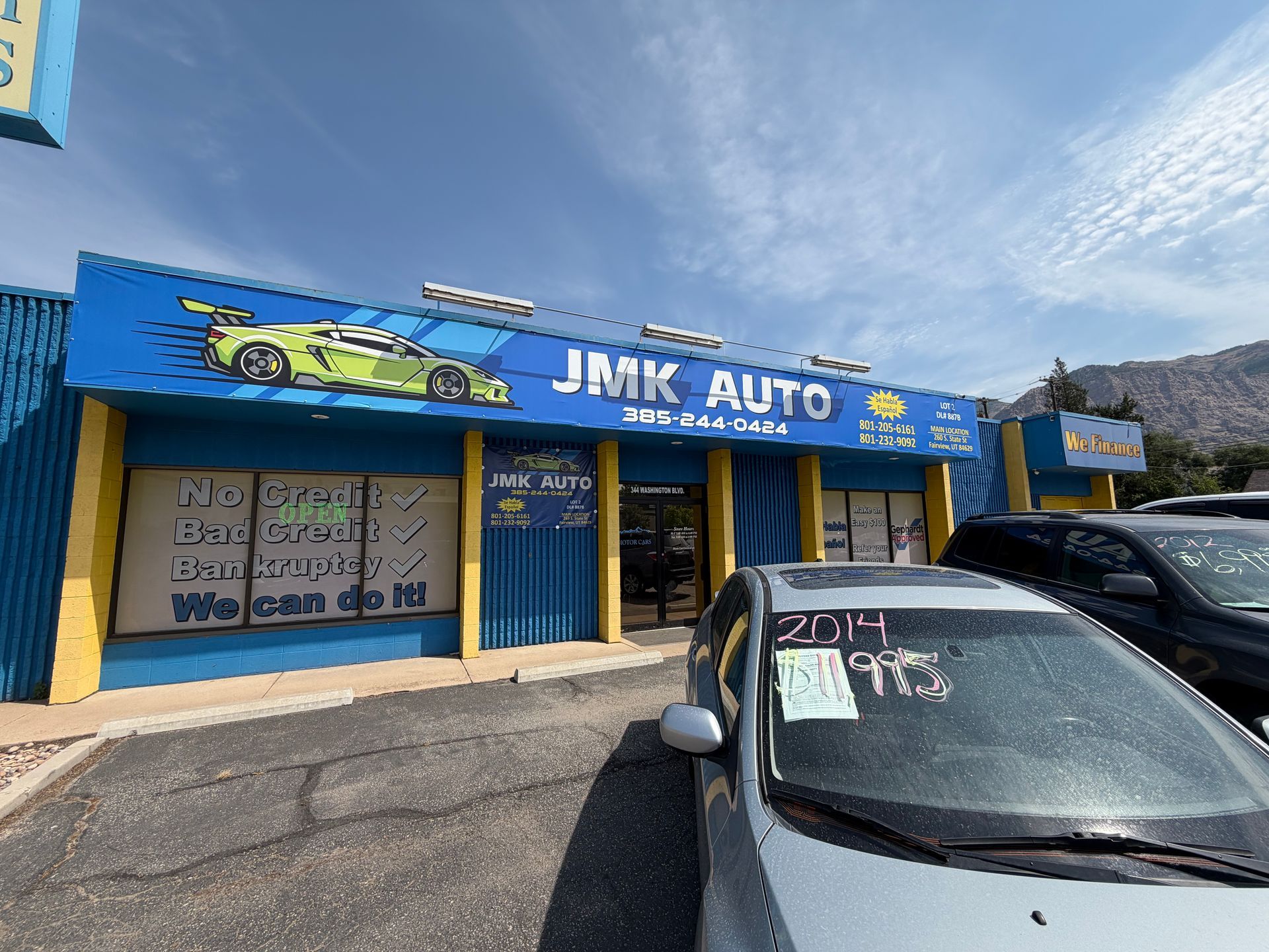 JMK Auto storefront with car graphics and parked vehicles under a sunny sky