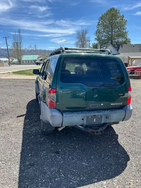 Damaged green SUV parked on a gravel lot under a blue sky