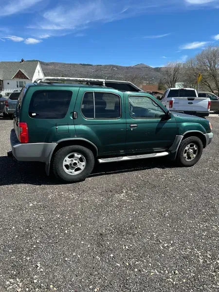 Green SUV parked on a gravel lot under a clear blue sky.