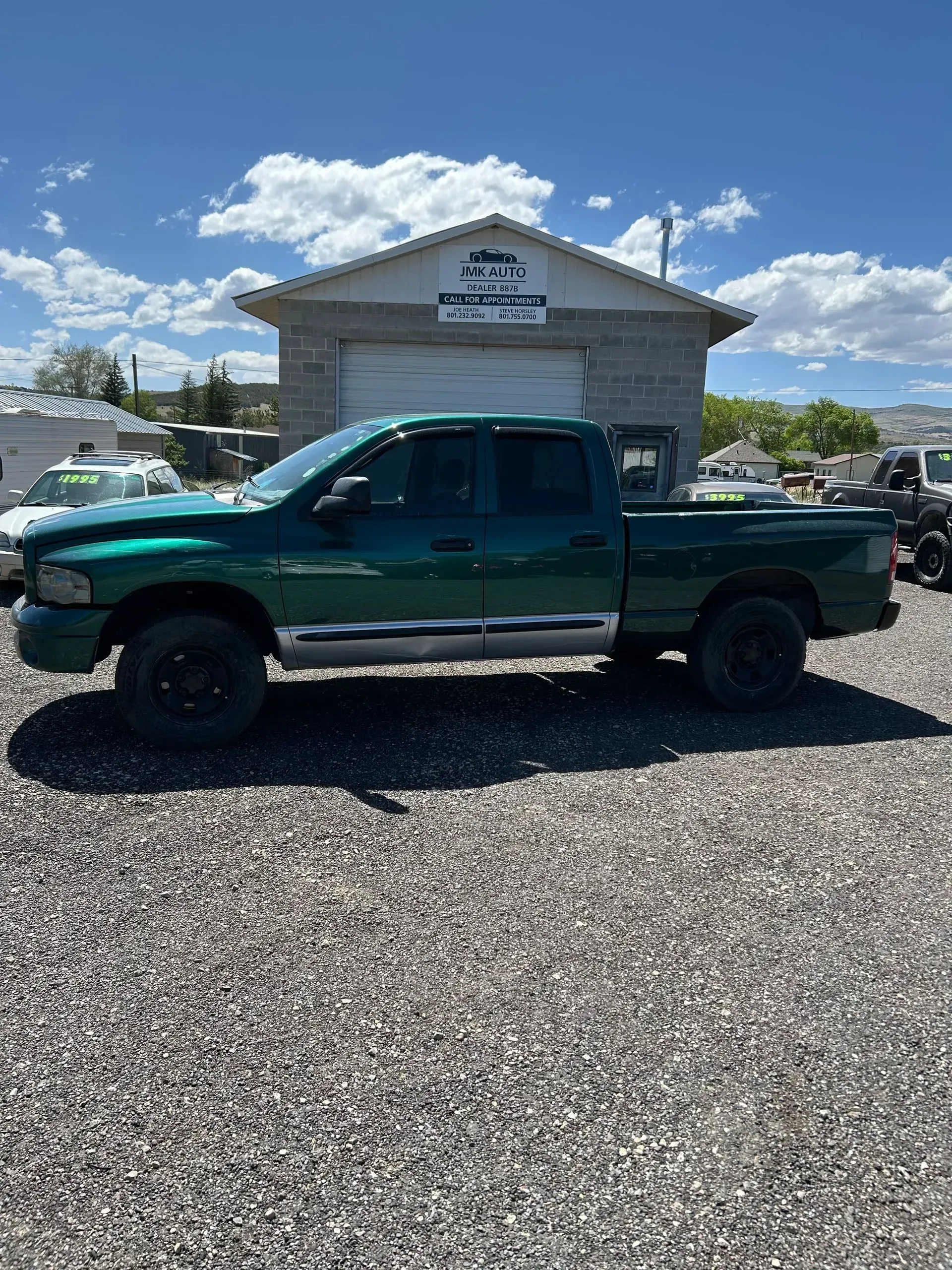 Dark green pickup truck parked on gravel in front of a small building under a blue sky.