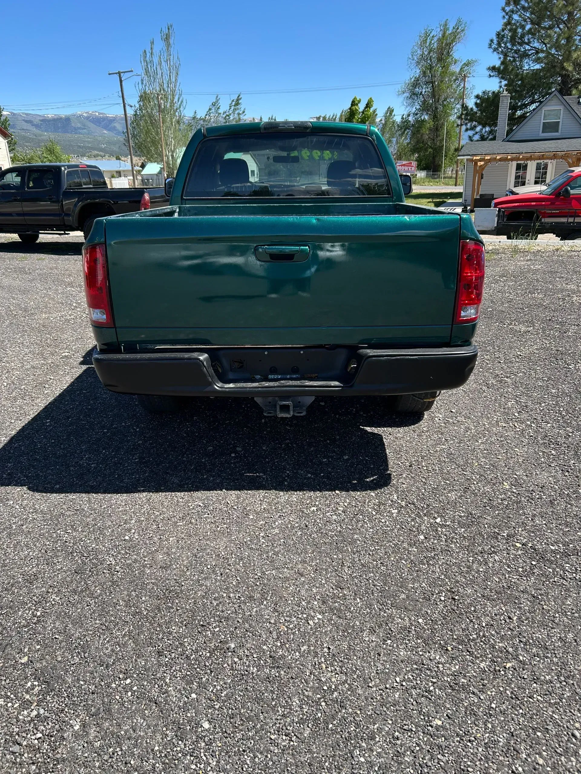 Green pickup truck parked on a gravel lot with mountains and trees in the background