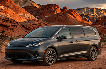 Dark gray minivan parked on rocky desert terrain with red sandstone cliffs in the background