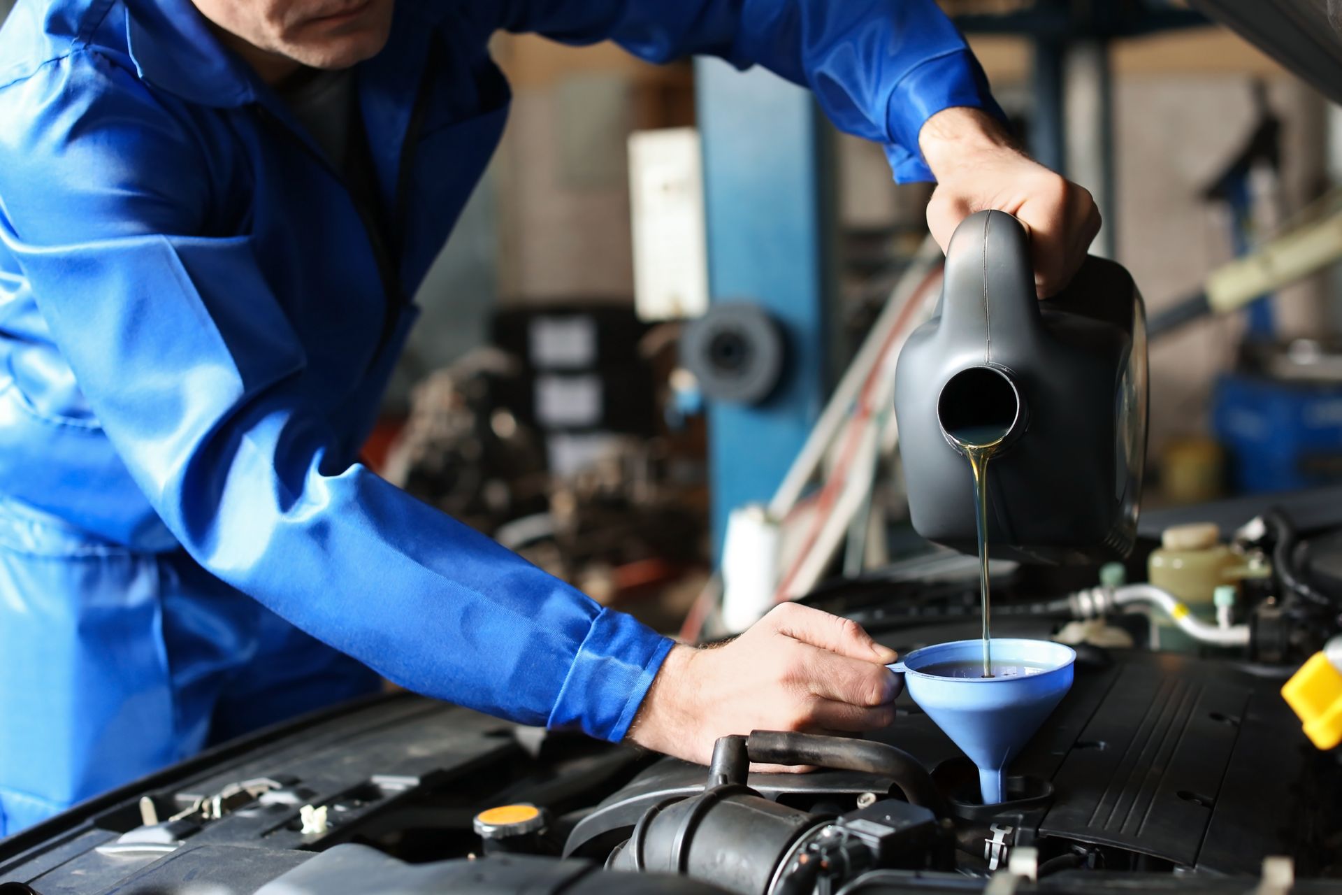 Mechanic in blue shirt pouring fluid into a car engine with a funnel