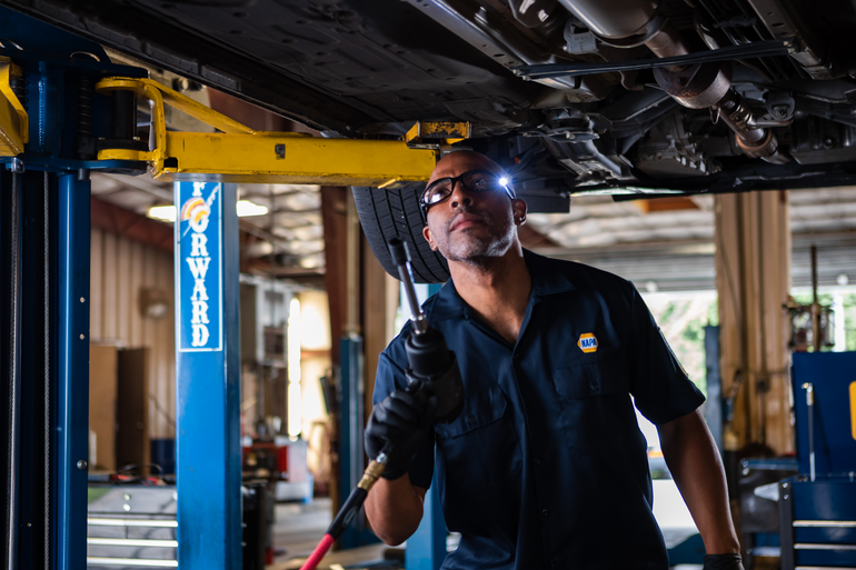 A mechanic with a headlamp works on a vehicle raised on a blue lift in an auto repair shop.