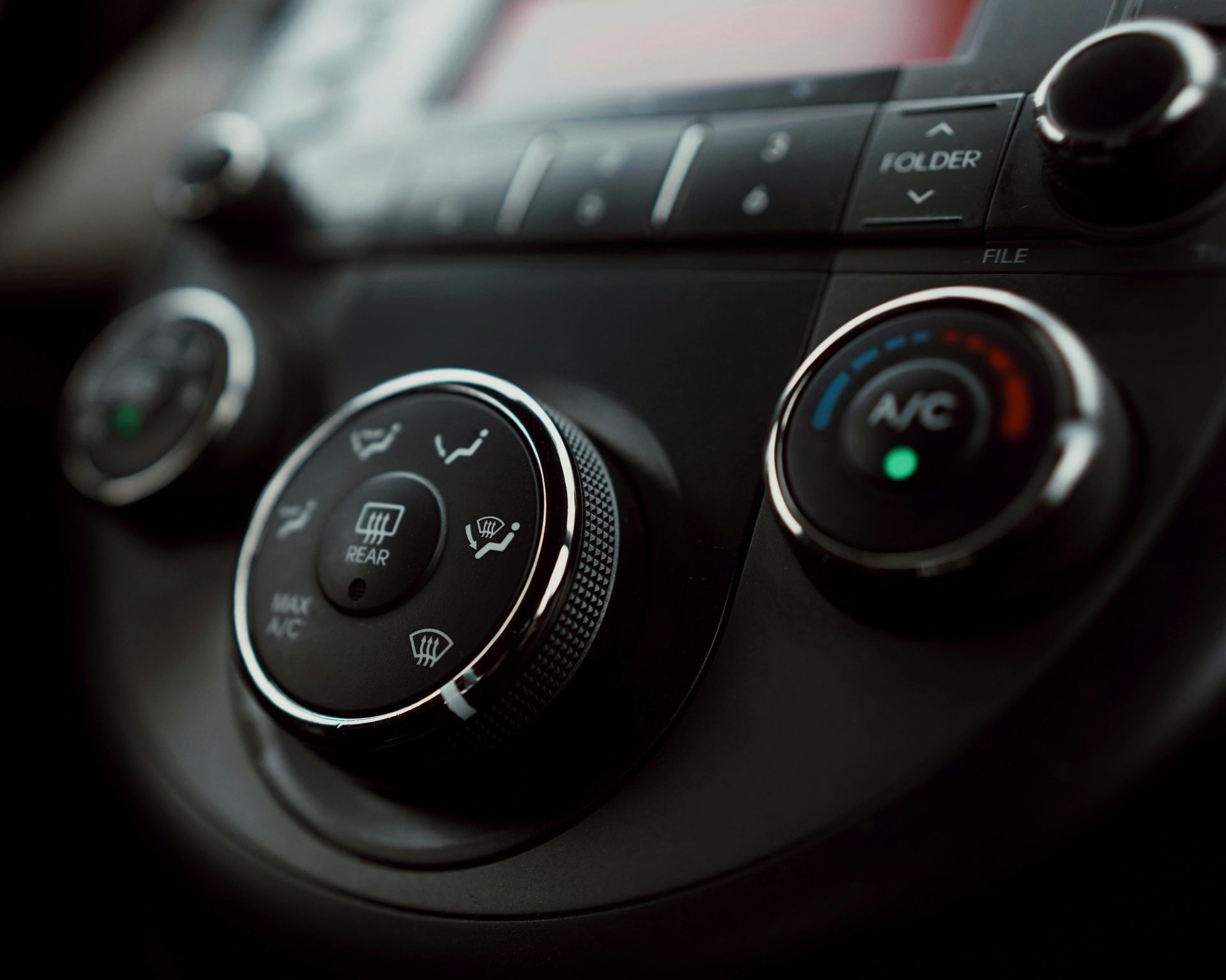 Car dashboard climate controls with circular knobs and illuminated A/C button in dark interior