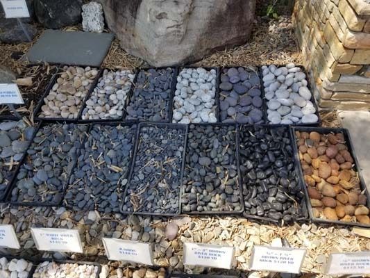 Display of decorative pebbles and stones in assorted colors arranged in rows outdoors