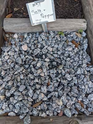 Pile of silver-gray salt rocks in a bin with a small handwritten price sign.