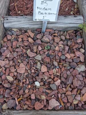 Red-brown bark chips beneath a small sign reading “#5 medium bark shavings”