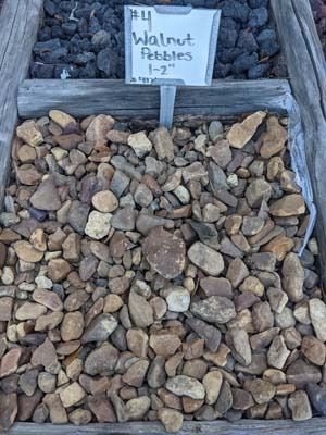 Bin of mixed tan and brown pebbles labeled “#4 Walnut Pebbles $2”