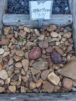 Stone pile with a small sign reading “Cornerstone 11-13” against a gravel and wood backdrop