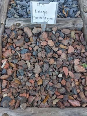 Piles of mixed brown and reddish rocks with a small sign reading “Large Riverstone” above them
