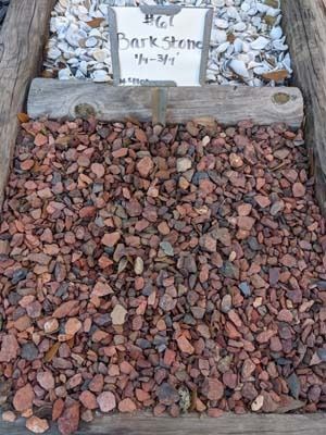 Gravel-covered memorial plaque with a small white marker at the top, bordered by stones.