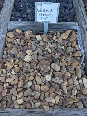 Sign reading “Walnut Pebbles 1-2” above a bin of mixed tan and brown rocks