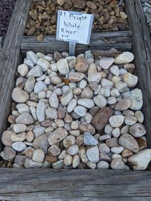 Pile of pale river rocks in a wooden frame with a small handwritten sign above it.