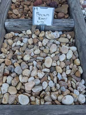 Decorative bed of smooth river rocks with a wooden sign reading “Stony River.”