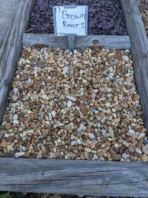 Small gravel-filled wooden frame with a handwritten sign reading “Brown River” at the top.
