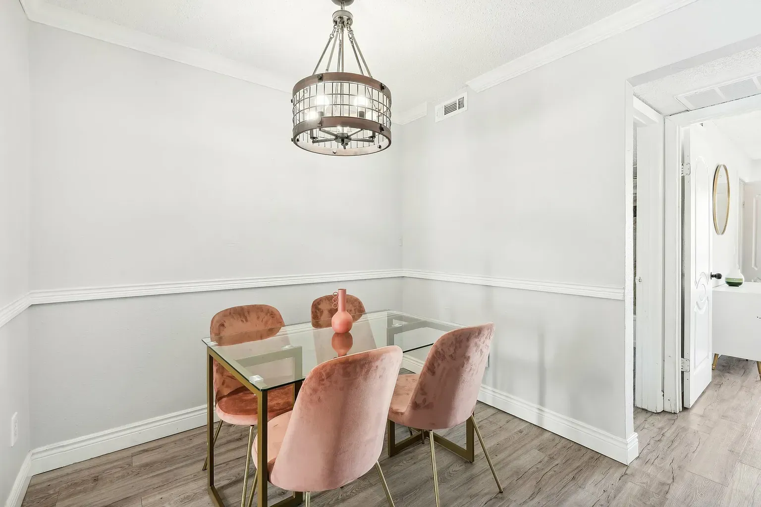 Dining nook with glass table and pink velvet chairs in a modern apartment, chandelier above.