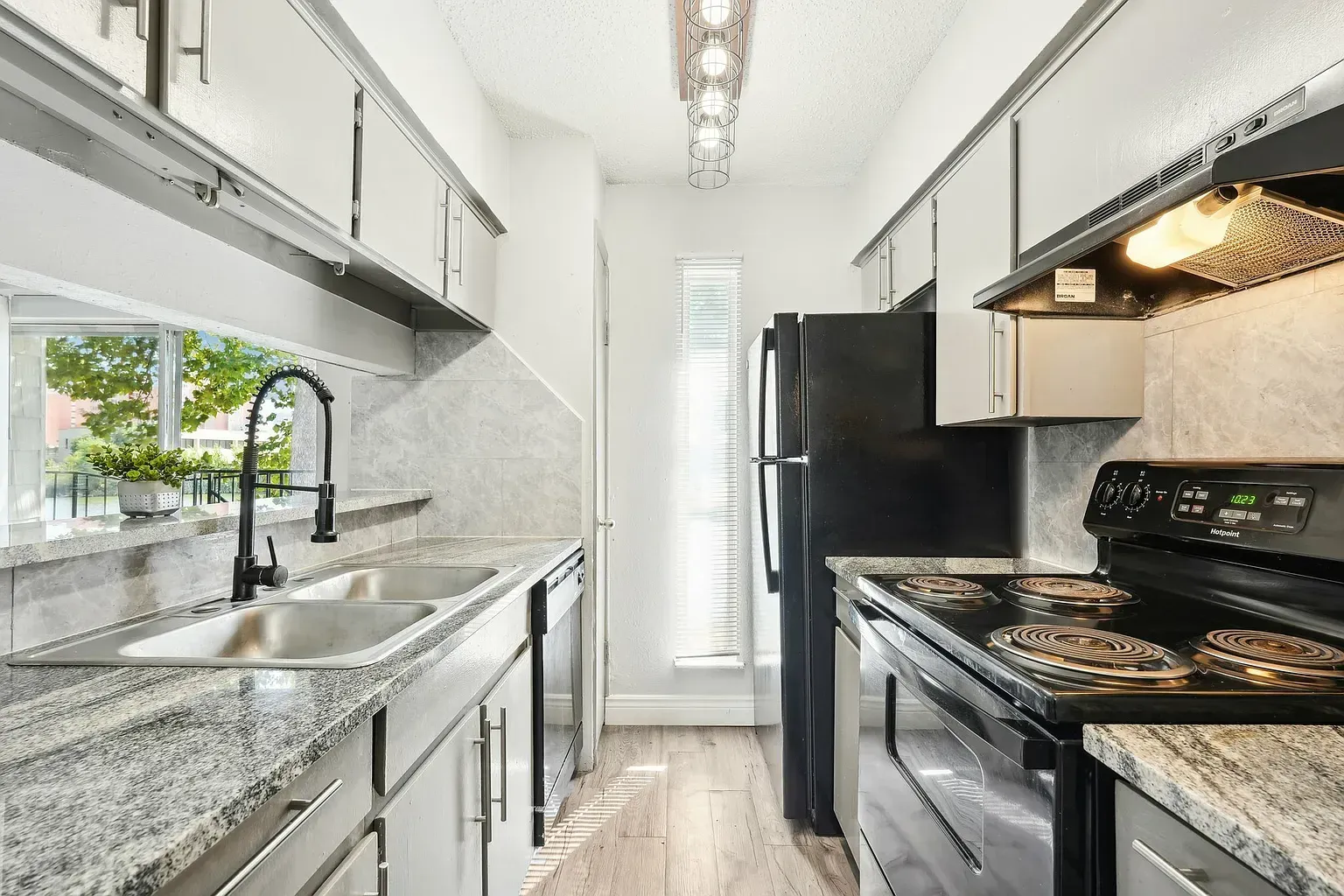 Narrow galley kitchen with granite countertops, double sink, and black appliances.