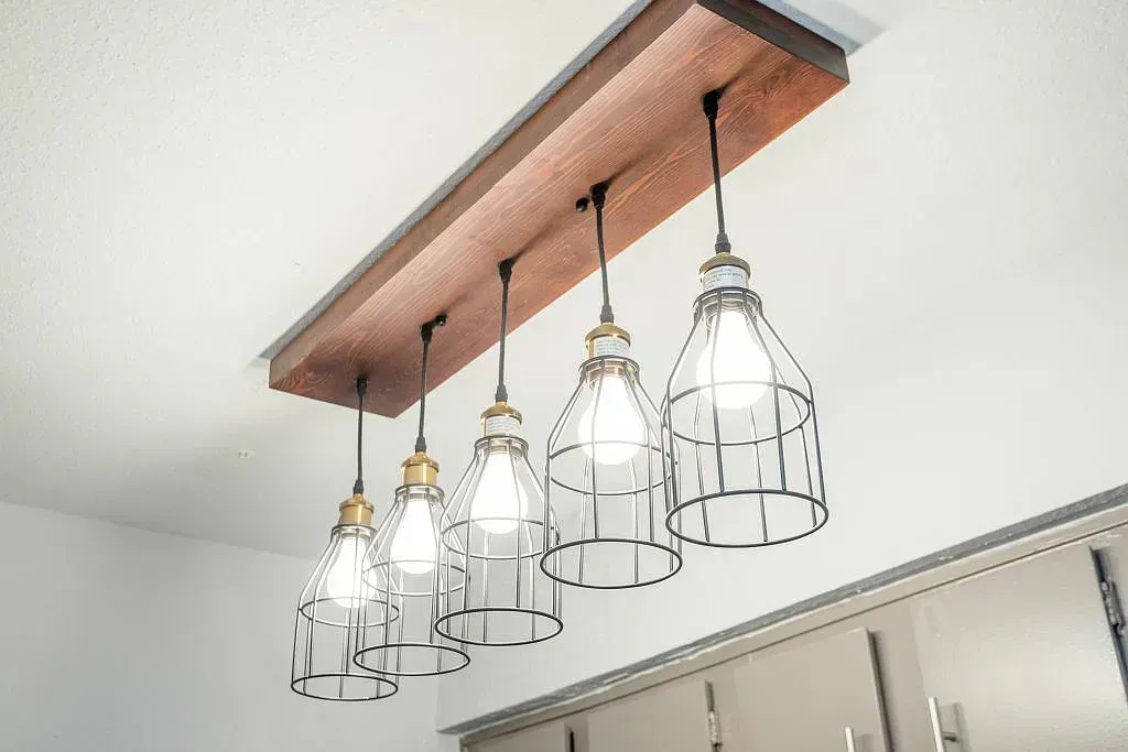 Industrial pendant lights with wire cages hanging from a wooden beam indoors.