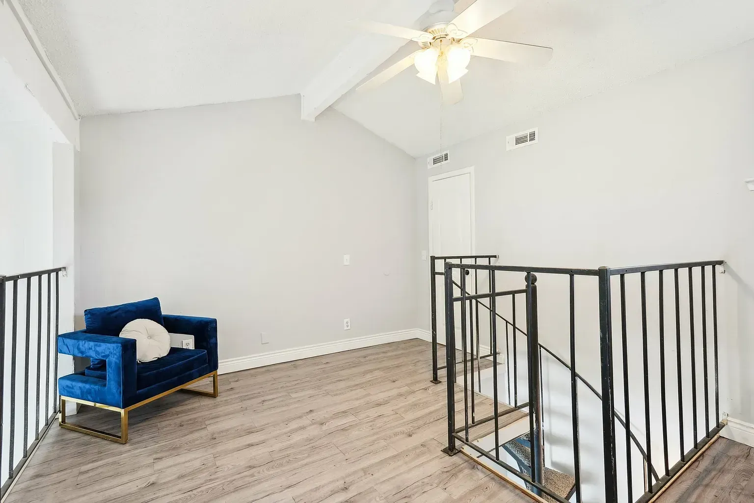 Loft-style upper-level living area with railing, white walls, a ceiling fan, and a blue armchair.