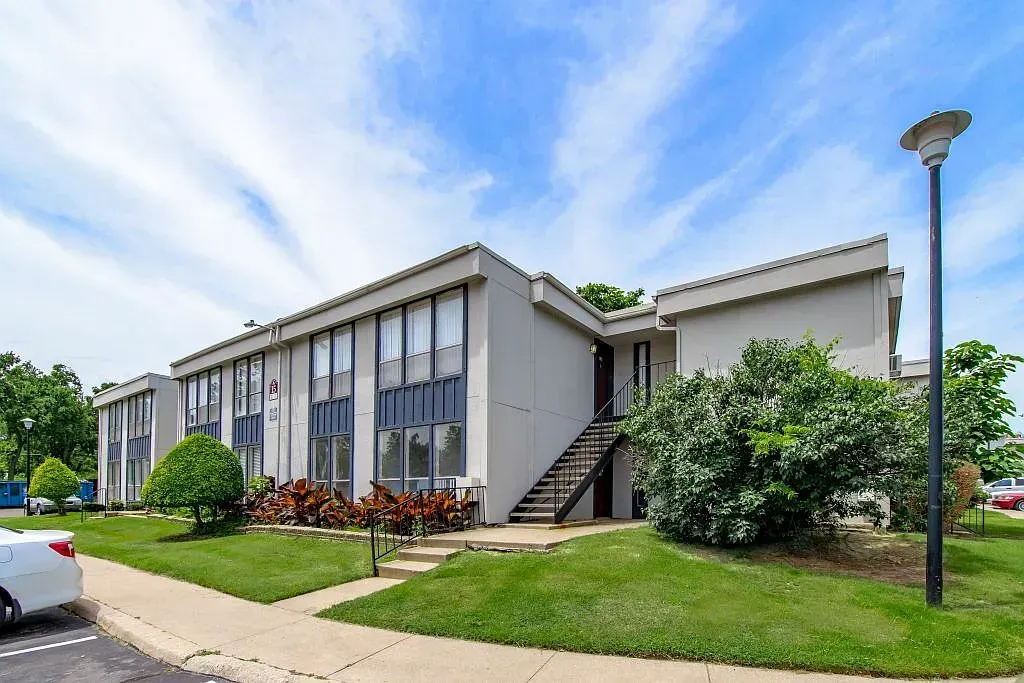 Exterior view of a two-story apartment building with stairs, landscaping, and a sidewalk.