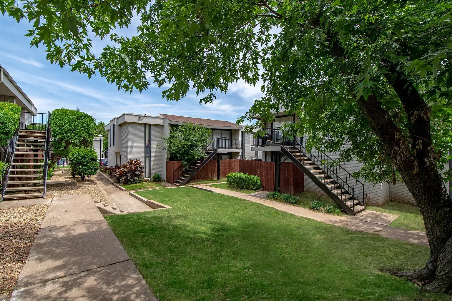 Exterior view of a multi-building apartment community with grassy courtyard, trees, and outdoor stairs.