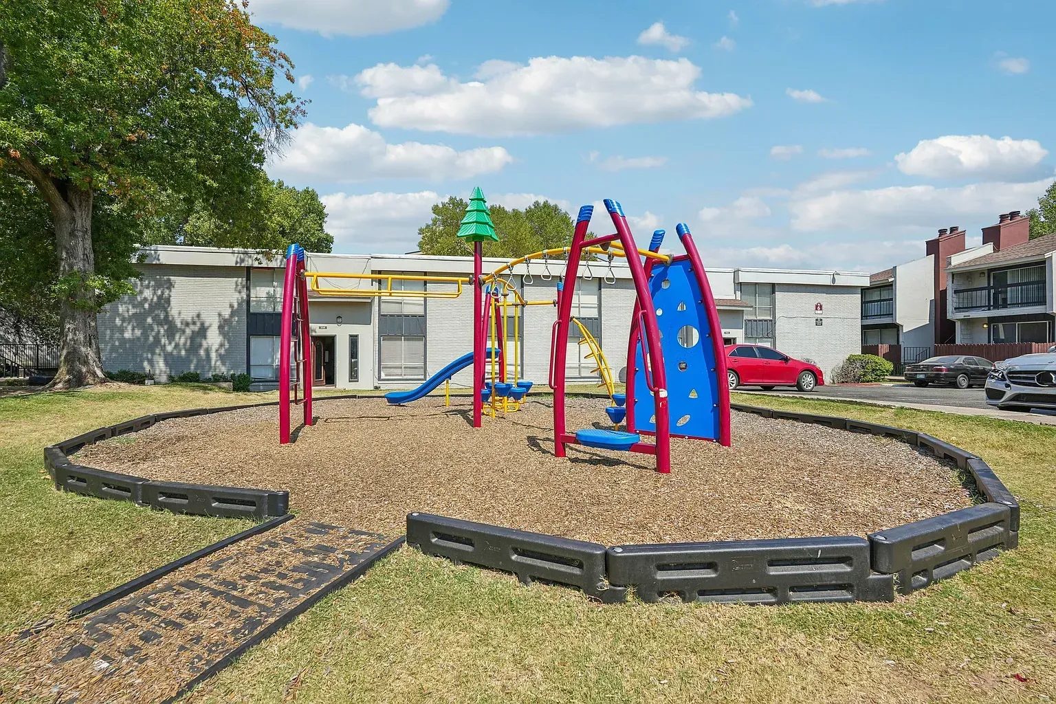 Colorful playground with slides and climbing structures in a courtyard, apartment buildings in the background.