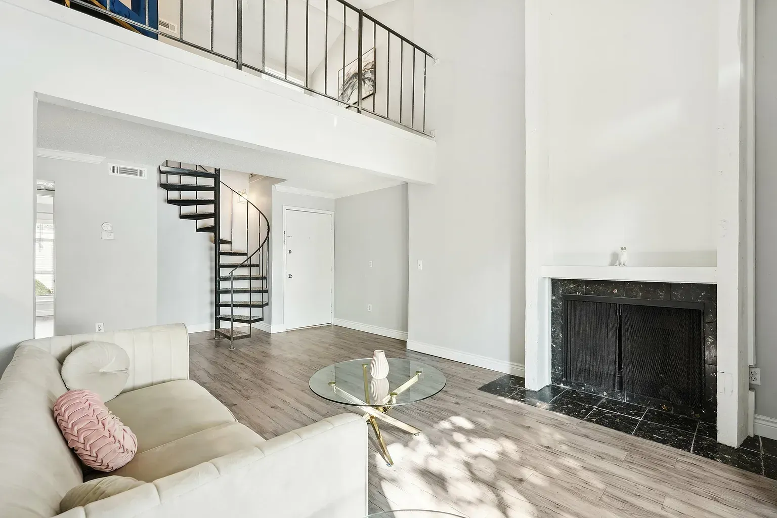 Bright living room in a modern apartment with a spiral staircase, mezzanine railing, and fireplace.