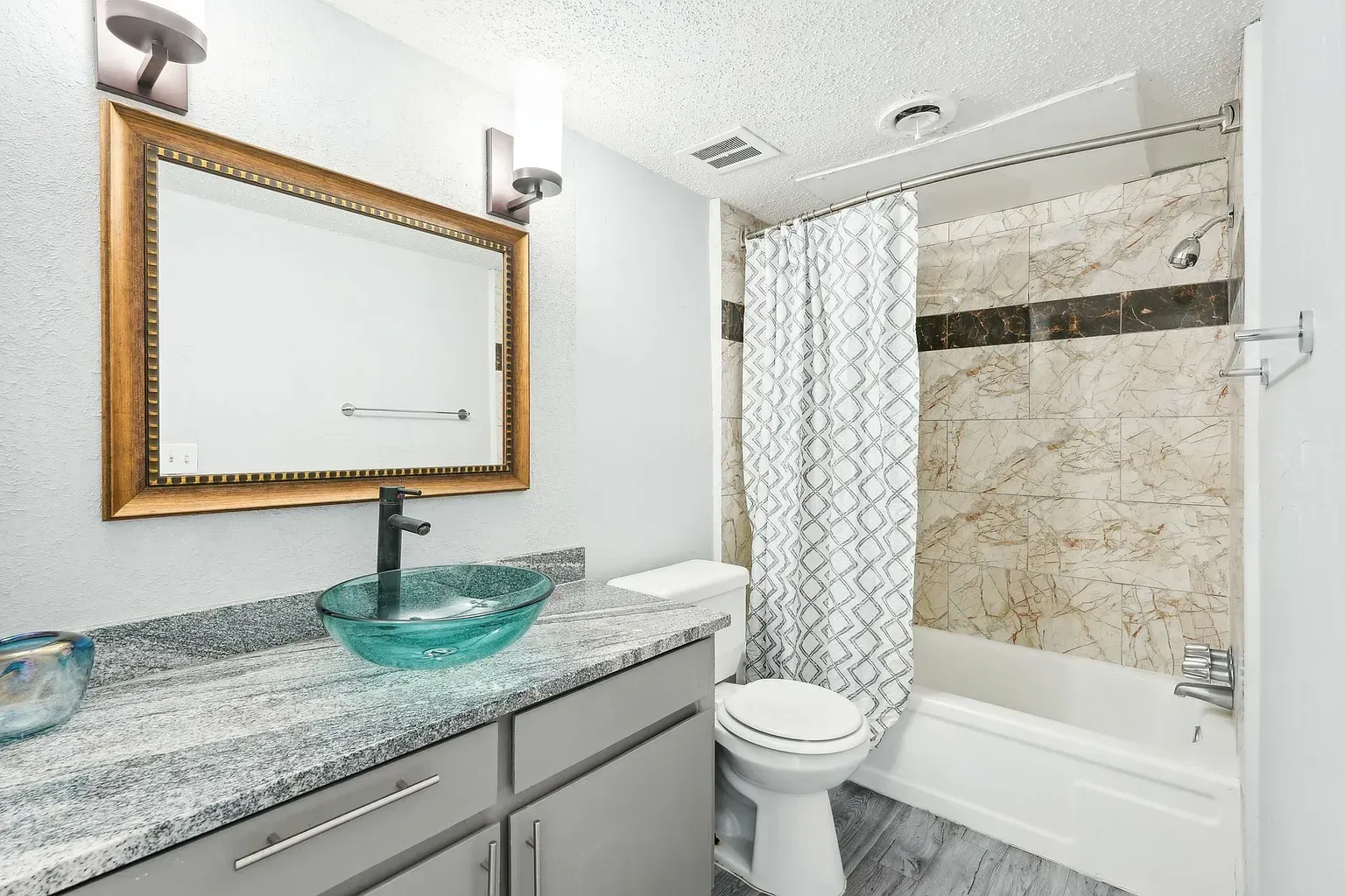 Modern bathroom with gray vanity, glass vessel sink, large framed mirror, and tiled shower.