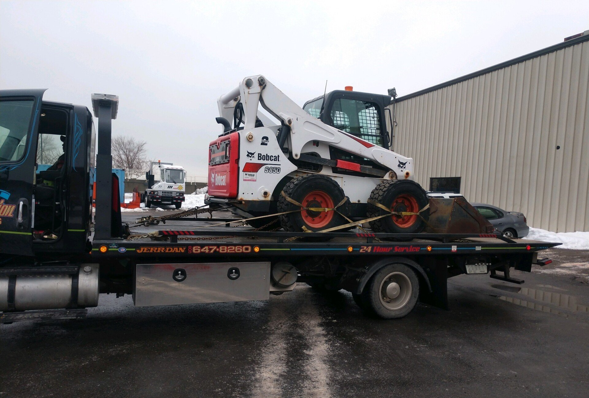 white dirt loader on the bed of a tow truck