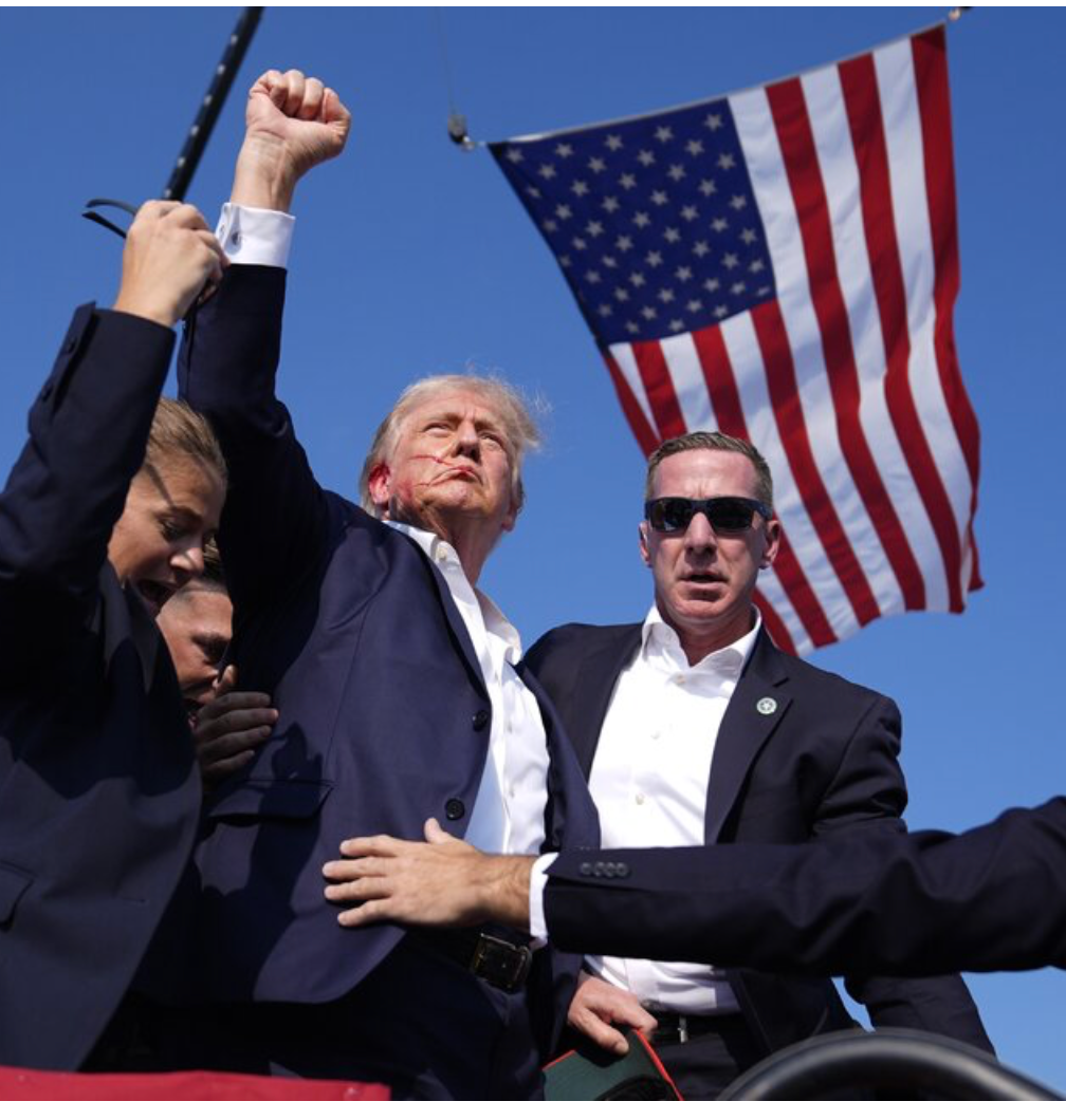 A man in a suit holds up his fist in front of an american flag