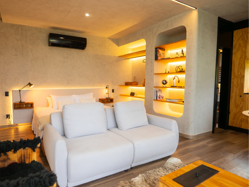Sala de estar moderna com sofá branco, iluminação aconchegante, prateleiras na parede e ar-condicionado de parede.
